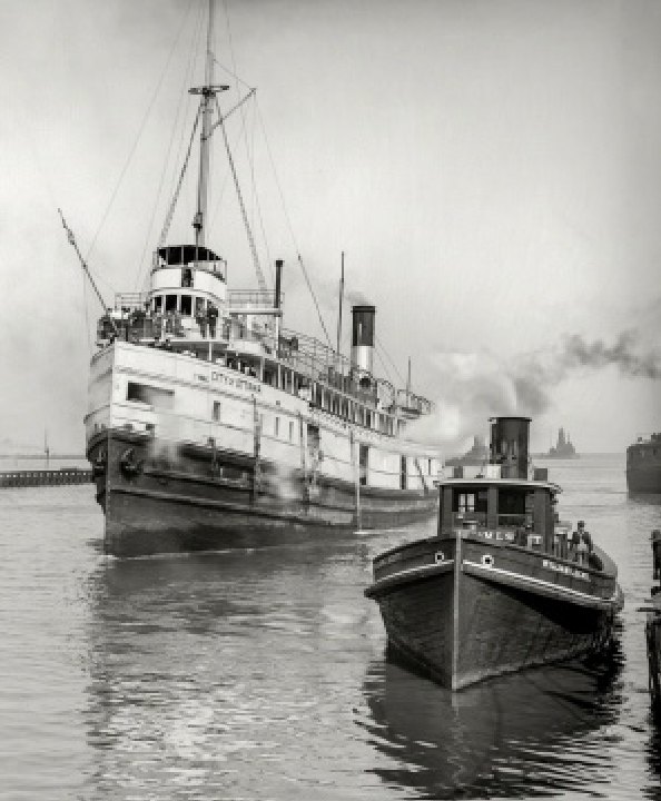 A steamship with tall masts and a smoking funnel, and a small tug beside it, on calm harbour water in a faded black-and-white photograph