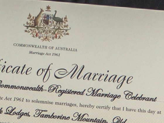 The top of an Australian marriage certificate held up by a couple, the coat of arms, its printed headings and the celebrant's script lines small and soft