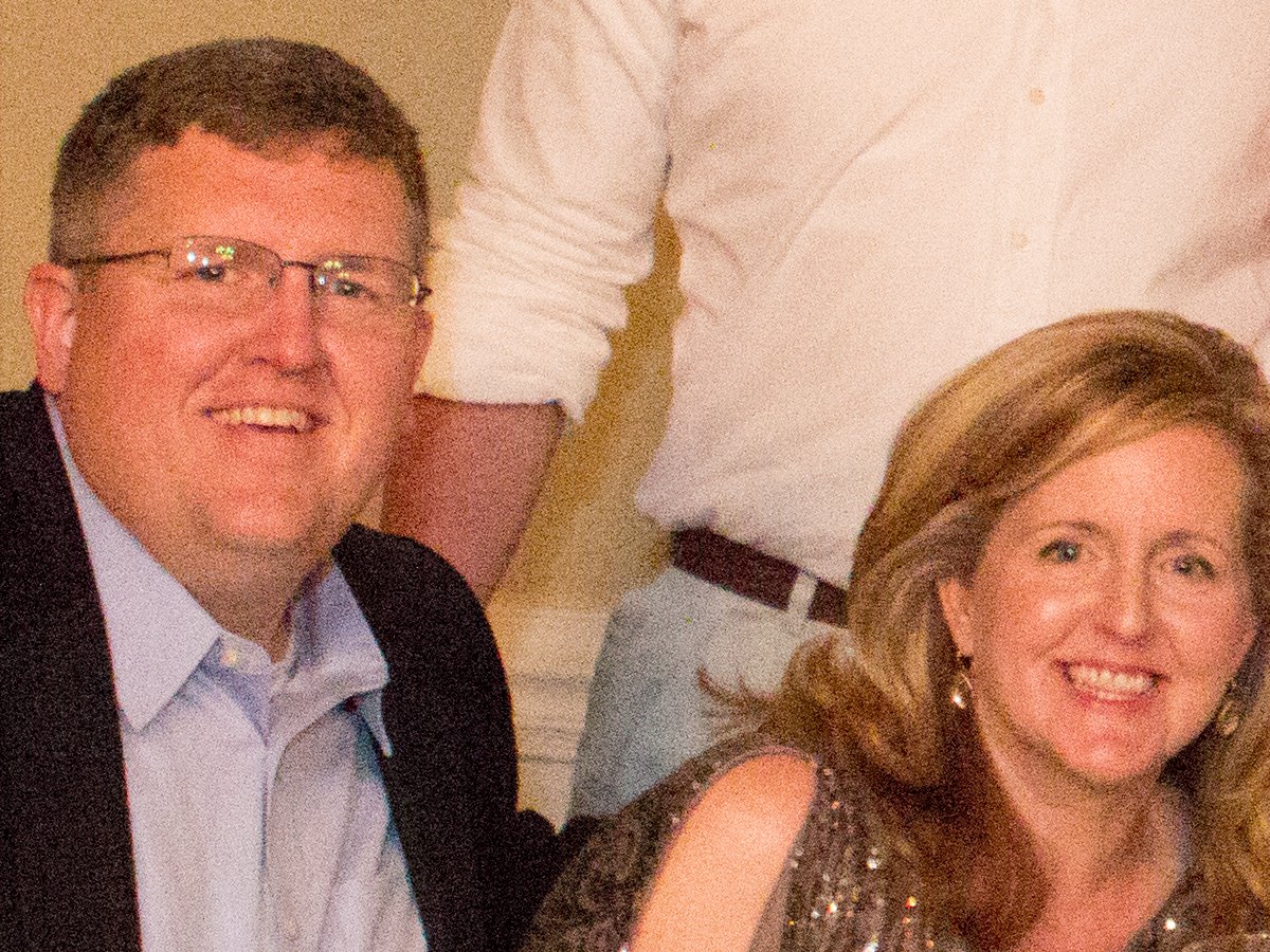 A smiling man in rimless glasses and a smiling woman with long fair hair at a reception table, covered in heavy coloured grain from a high ISO